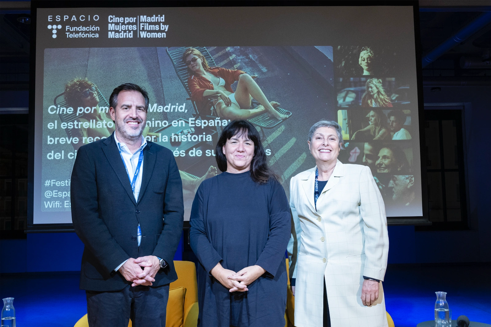 Pilar Castro, María Adell y Pablo Gonzalo posando frente a la cámara en un evento, con una proyección en el fondo.