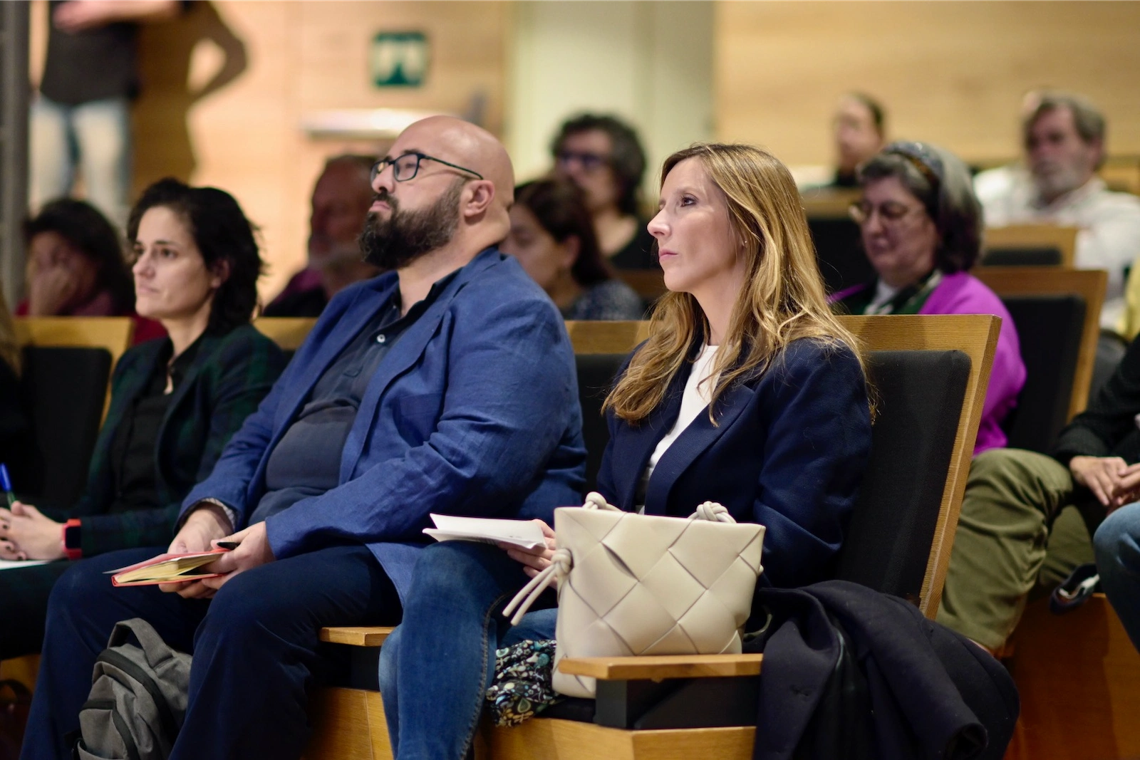 Público asistente al Encuentro TELOS escucha atentamente la conversación; en primer plano, una mujer y un hombre sentados en la primera fila sostienen cuadernos, rodeados de otras personas concentradas en la charla.
