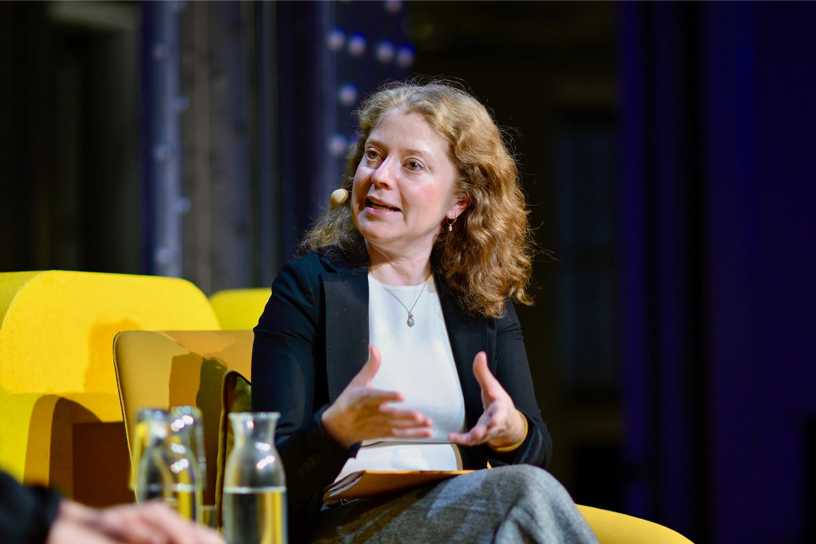 Eva Catalán, sentada en el escenario del auditorio, habla con expresividad mientras gesticula con las manos durante su participación en el Encuentro TELOS. Lleva micrófono de diadema y una carpeta en el regazo