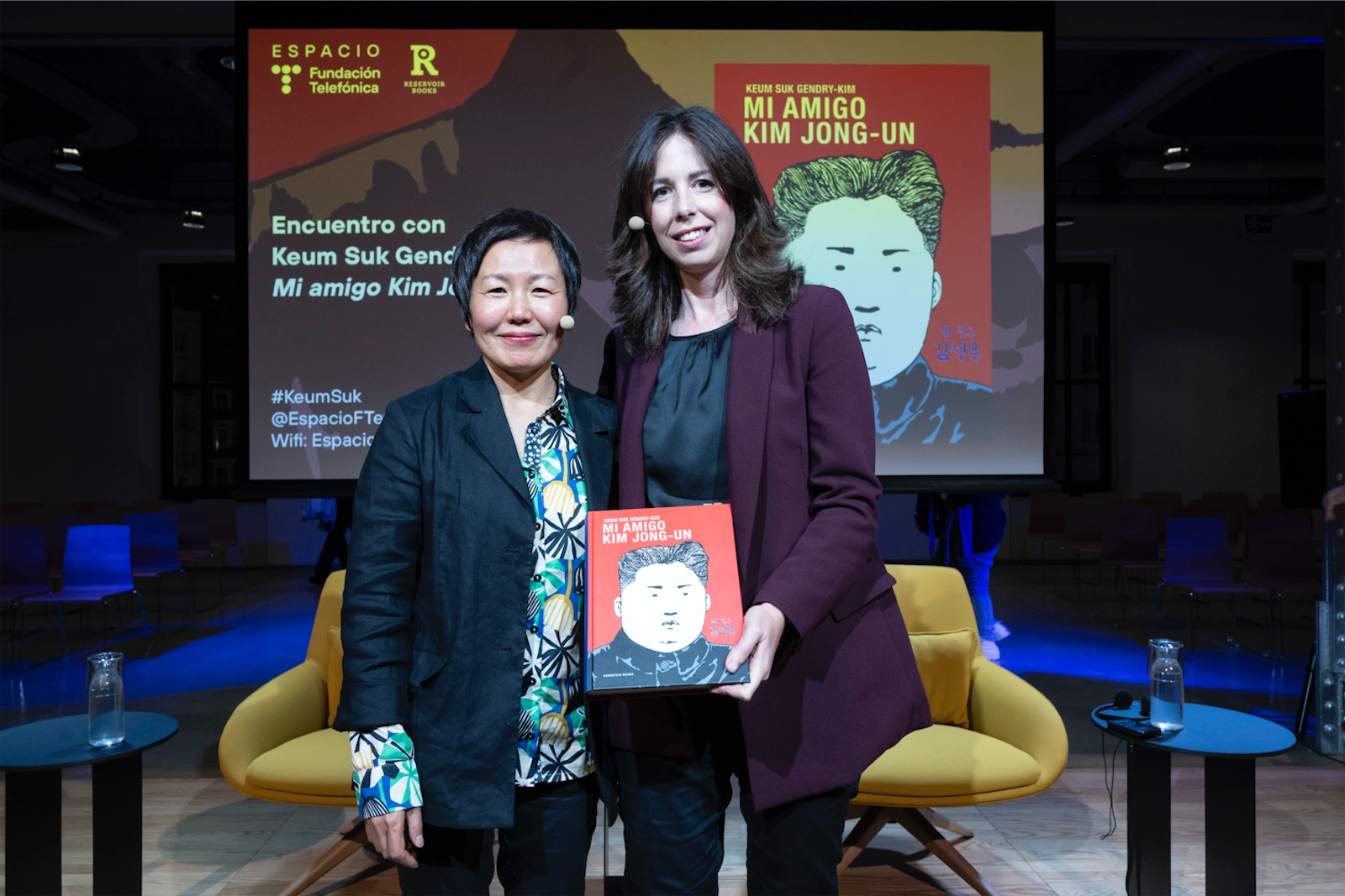 Keum Suk Gendry-Kim y Sara Romero posan juntas al final de la entrevista, mostrando el libro Mi amigo Kim Jong-un. Ambas están sonriendo mientras sostienen el libro frente a ellas.