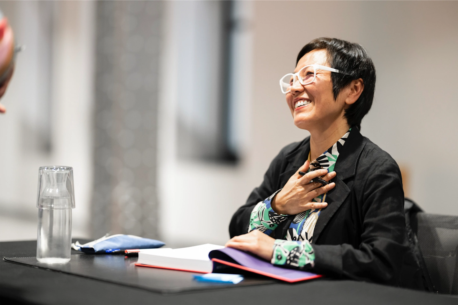 Keum Suk Gendry-Kim sonríe con alegría mientras firma un libro para un lector. La autora parece emocionada y agradecida mientras recibe una interacción cálida de su público.