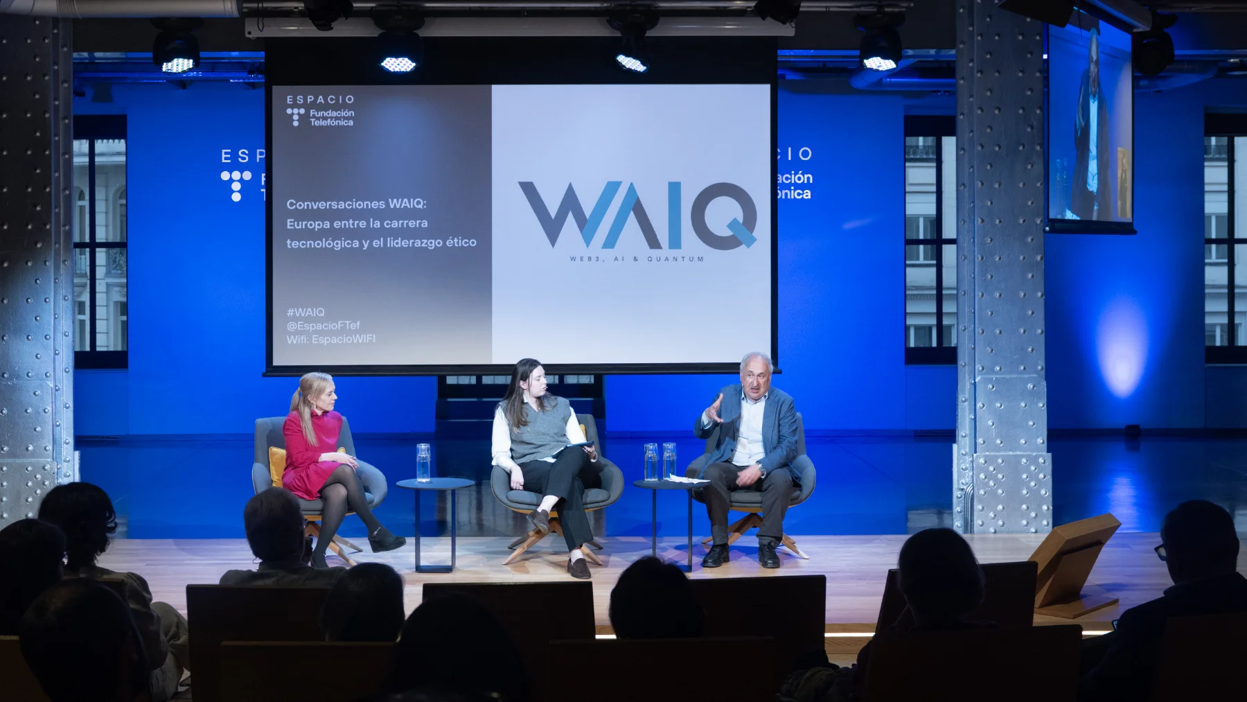 Escenario con tres personas en uno de los encuentros Conversaciones WAIQ